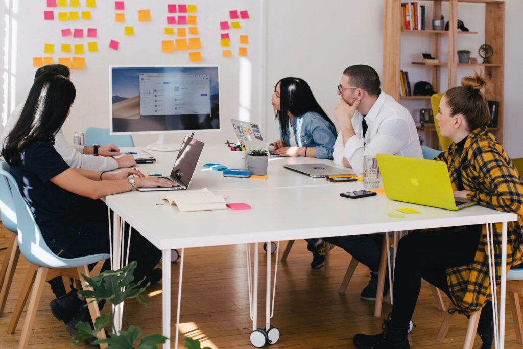 Workers against a whiteboard gathered around a table looking at screens.