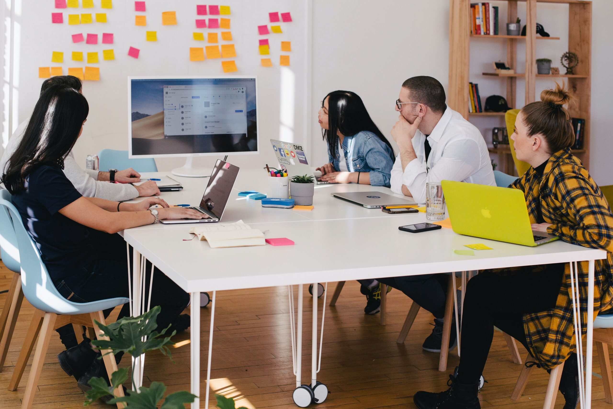 Workers against a whiteboard gathered around a table looking at screens.