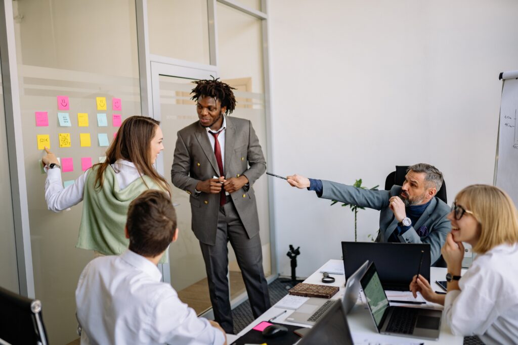 Office workers gathered around the table in a gray conference room, discussing ideas on post-its