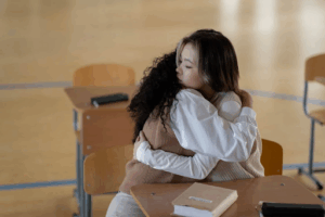 A female consoles a student in a classroom setting